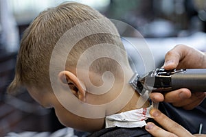 The barber& x27;s hand shaves the hair on the back of the child& x27;s head in a beauty salon The child is given a light