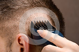 A Barber`s hand with a young man`s hair clipper. Create a stylish men`s haircut in a Barbershop or at home. Men`s haircut proc