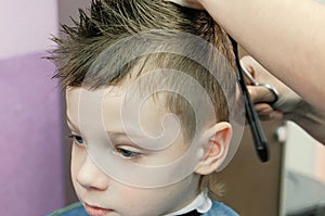 Barber`s hands combs and cutting blond short boy`s hair with scissors. Closeup boy`s face.