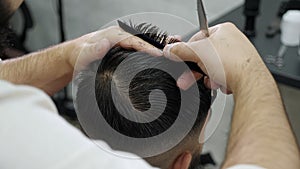 A barber's hands with scissors and a comb, he cuts a man's hair in a barbershop.