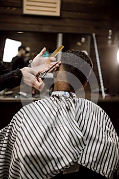 The barber scissors hair on the sides for a stylish black-haired man in the barbershop. Men`s fashion and style