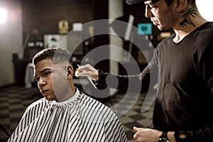 The barber scissors hair on the sides for a stylish black-haired man in the barbershop. Men`s fashion and style