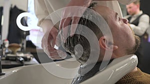 Barber shampooing washing a male client's head in the sink.