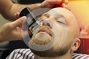 Barber shaves beard of client man on chair Barbershop. Beard Haircut. barber shaving beard with electric razor in vintage barber s