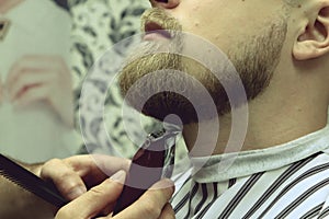 Barber shaves beard of client man on chair Barbershop. Beard Haircut. barber shaving beard with electric razor in vintage barber s