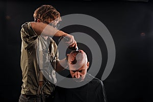 The barber shaves his head bald elderly man in the studio