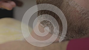 Barber shaves a man's beard, shaving with a straight razor, blade, close-up, side view, macro