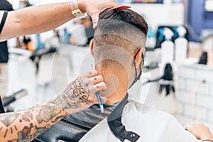 Barber shaving the hair of the nape of a man siting in a chair in a barber shop