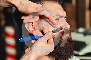 Barber shaving man with straight razor, close up. Handsome guy is getting shaved in barbershop. Barber shop