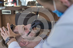 Barber shaving a young bearded barber shop customer guy with a razor. close up. beard haircut, dangerous razor, professional hair