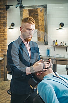 Barber Shop Studios. Barber shaving a bearded man in a barbershop. Beard man visiting hairstylist in barber shop