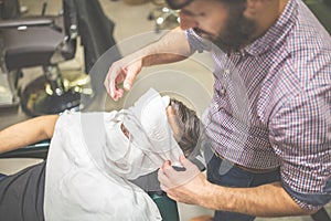 Barber softening male face skin with hot towel at barbershop