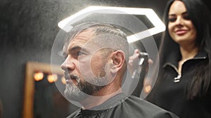 Barber sprays water on client hair before haircut and styling in barbershop. Hairdresser woman wets hair by spray and