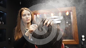 Barber sprays water on client hair before haircut and styling in barbershop. Hairdresser woman wets hair by spray and