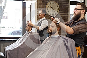 Barber styling beard with scissors to client at barbershop