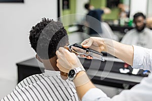 Barber trim hair with clipper on young unshaven black man in barbershop studio. Professional hairdresser cut hair with electric