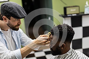 Barber trim hair with clipper on young unshaven black man in barbershop studio. Professional hairdresser cut hair with electric