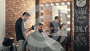 Barber trimming hair of smiling male client in barber shop