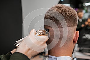 Barber trims the back of a mans head with a trimmer at the barbershop.