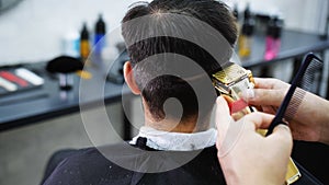 Barber uses an electric razor to make a contour on the back of the client's head in a barbershop.