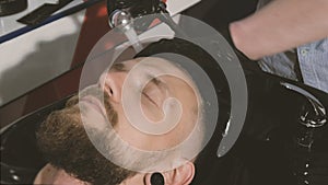 Barber washing man head in stylish barbershop