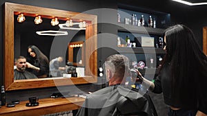 Barber woman cuts bearded man`s hair with a clipper in barbershop. Men`s hairstyling and hair cutting in salon. Grooming