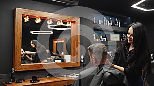 Barber woman cuts bearded man`s hair with a clipper in barbershop. Men`s hairstyling and hair cutting in salon. Grooming