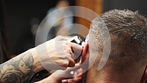 Barber woman cuts bearded man`s hair with a clipper in barbershop. Men`s hairstyling and hair cutting in salon. Grooming