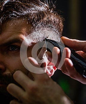 Barber works with hair clipper. Hipster client getting haircut. Hands of barber with hair clipper. Haircut concept