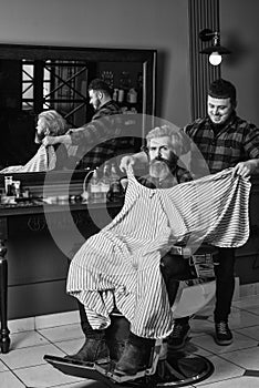 Barber works on hairstyle for bearded man barbershop background. Hipster client getting haircut. Barber and hair stylist