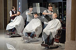 Barbers grooming and styling haircuts of clients in barbershop.