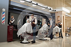 Barbers working with clients in modern barbershop. photo