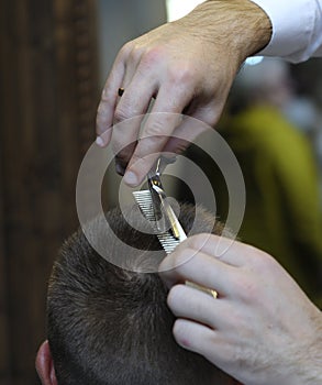 At a barbershop. Barber hands cutting customer hair with scissors and comb