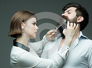 Barbershop or hairdresser concept. Woman hairdresser cuts beard with scissors. Guy with modern hairstyle visiting