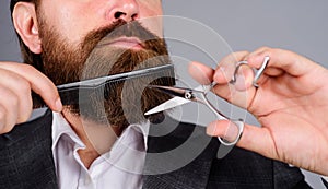Barbershop procedures. Professional beard care. Stylish bearded man in suit cutting his beard and mustache with scissors