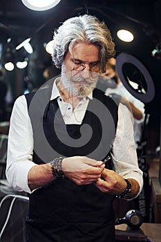 In barbershop. Stylish modern senior man with gray hair and beard is indoors