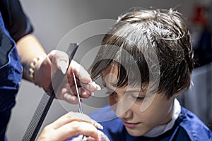 barbeshoper cuts the bangs under the comb on the wet hair of the little boy.