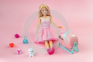 Barbie doll with loose blond hair in a pink dress standing on a blue background. barbie mother with a baby in bed