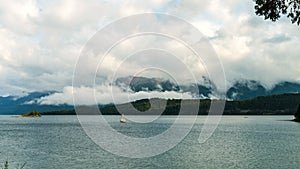 Sailboat navigating a calm lake with low clouds and mountains in the background. Villa La Angostura, Argentina photo