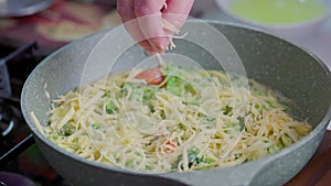 bare caucasican woman hand sprinkling roasting vegetable omelette with grated cheese stripes