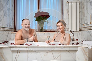 Bare-chested man and his charming wife soak in rose-petal bath