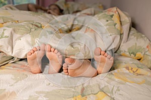 bare, clean feet of siblings, lying side by side under same blanket on the bed