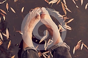 Bare feet above the dark water. Yellow autumn leaves float in the lake.