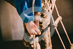 Bare feet of a boy holding on to a rope while climbing up it