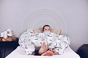 Bare feet. The boy is lying in bed covered with a blanket. Foot and heel.