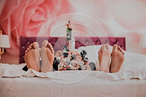 Bare feet of the bride and groom lie on a pink blanket between them lies a wedding flower bouquet