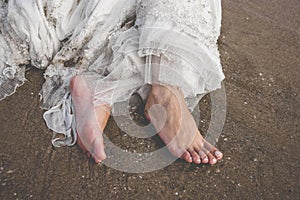 Bare feet of a bride with her messy dress on the beach