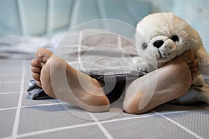 bare feet of a child on a bed under a blanket, on one foot lies a soft fluffy toy seal