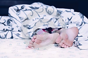 Bare feet of a child. A child in pajamas. Bare feet sticking out from under the blankets. The boy is sleeping in bed. Foot