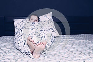 Bare feet of a child. The child's legs look out from under the blanket. Foot